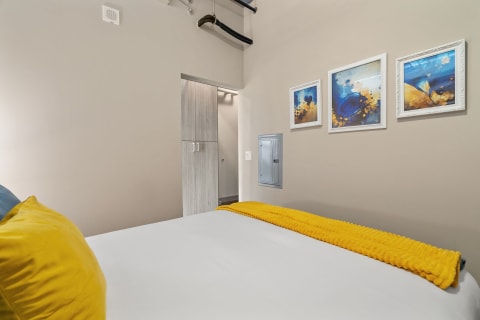 Cozy bedroom featuring a white bed with a yellow throw blanket and blue pillow, along with framed artwork on the wall.