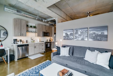 Modern studio apartment interior featuring a gray sofa, kitchen area, and city skyline artwork.