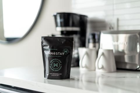 A bag of MINNESTAY coffee on a kitchen countertop with a black coffee maker and white mugs in the background.