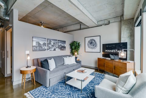 A contemporary living room with gray furniture and blue rug, showcasing urban artwork and a television.