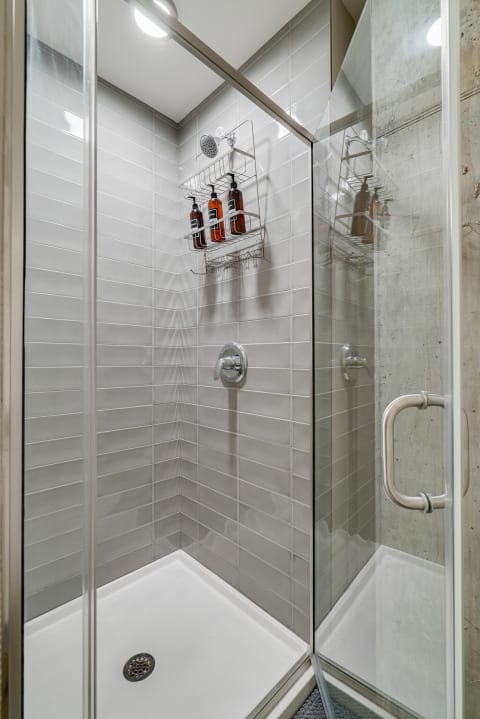 Modern shower stall with gray tiles and amber bottles on a wire rack.