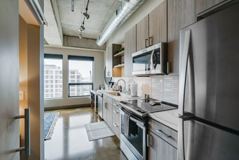 Modern kitchen with stainless steel appliances and large windows in an apartment.