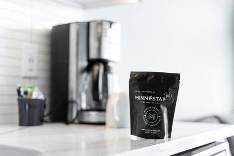 A black coffee package labeled 'MINNESTAY' on a marble countertop next to a coffee machine.