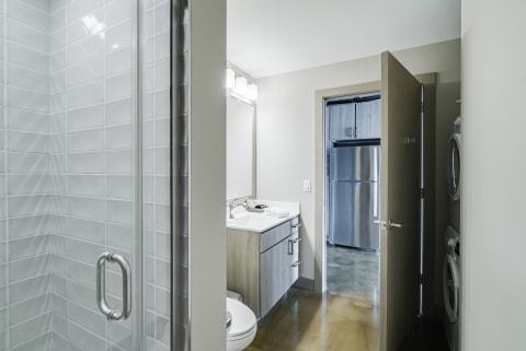 Contemporary bathroom with glass shower and view of kitchen appliances.