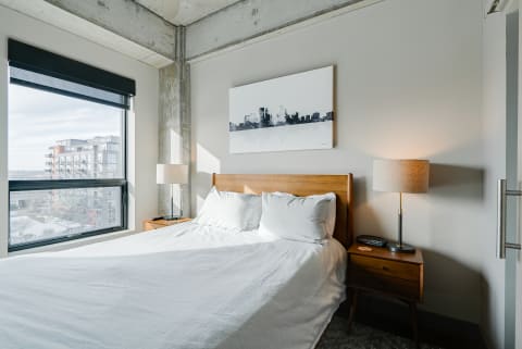 A cozy bedroom featuring a bed, artwork, and a view of neighboring buildings outside.