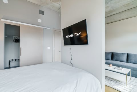 A stylish room with a bed, TV displaying 'MINNESTAY', closet, and sofa.