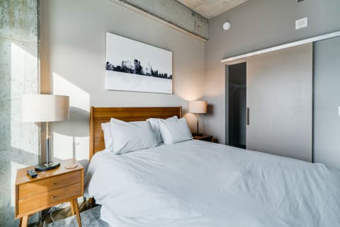 A stylish bedroom featuring a wooden bed, gray bedding, and a cityscape painting on the wall.