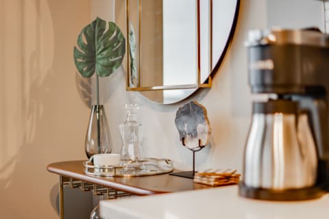 Stylish countertop featuring a coffee maker, mirror, and decorative elements including a plant and stone art.