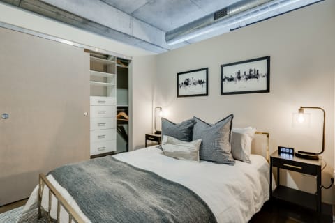 A stylish bedroom with a double bed, decorative pillows, and a sleek nightstand with a lamp.