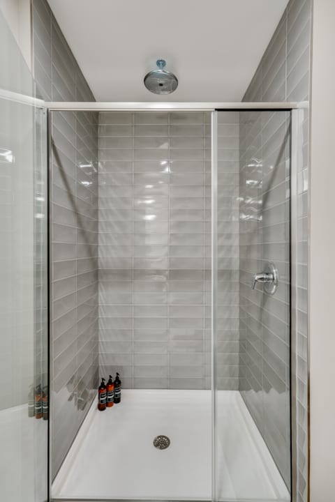 A modern shower area featuring gray tiles and a glass door, with shower products lined up at the corner.