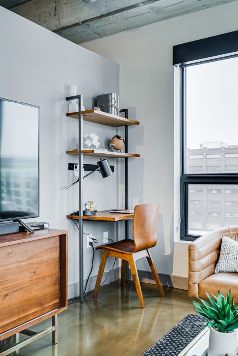Stylish corner workspace with wooden desk, shelves, and a leather sofa.