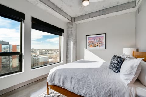 Modern bedroom with large windows and minimalistic decor, showcasing a city view.