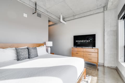 Modern bedroom with a queen bed, wooden dresser, and flat-screen television.