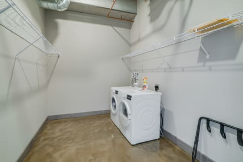 A simple and functional laundry room with white washing machines and open shelves.