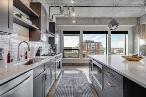 Modern kitchen with gray cabinets, a large island, and large windows overlooking the city.