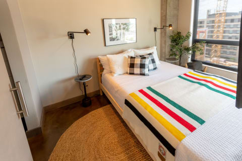 A modern bedroom featuring a colorful blanket on a bed, bedside table, and lamp.