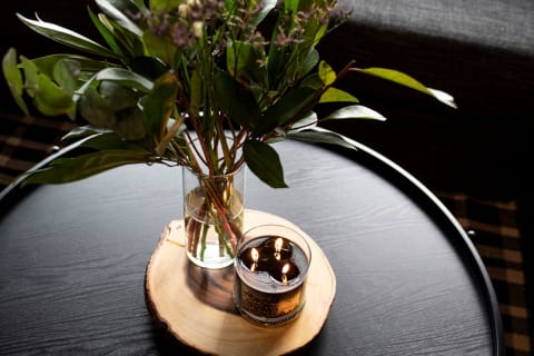 Tabletop with a glass vase of foliage and a candle on a wooden slice.