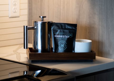 French press, coffee bag, and white ceramic cup on a wooden tray in a modern kitchen setting.