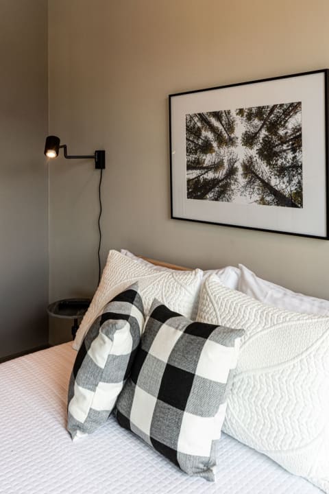 Cozy bedroom with a quilted bedspread, decorative pillows, and a black wall lamp.