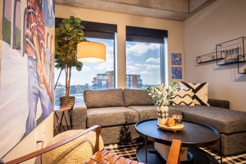 Cozy living room with a gray sectional sofa, black coffee table, and urban view through windows.