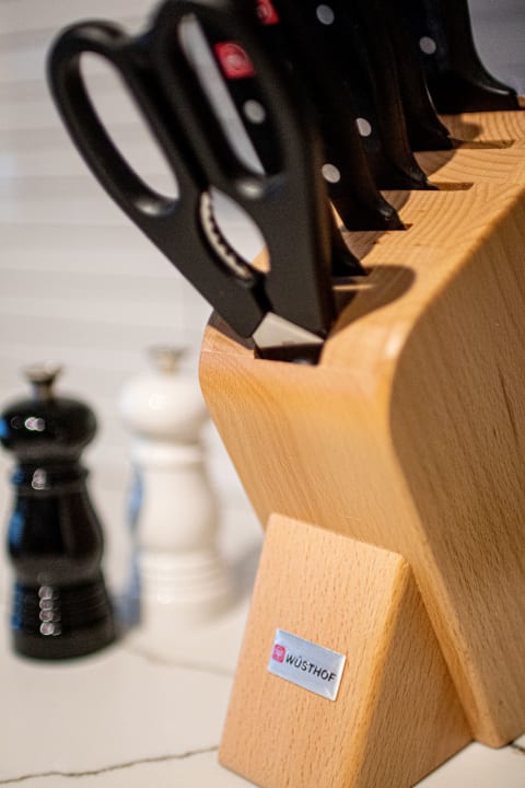 A knife block with scissors and a selection of knives in a modern kitchen setting with pepper grinders in the background.