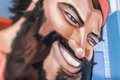 A close-up of a colorful mural showcasing a smiling man with a beard and a red cap against a blue background.