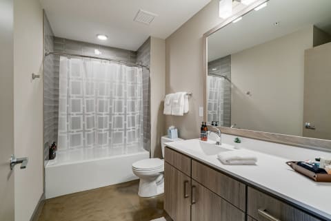 A contemporary bathroom with a bathtub, shower curtain, wooden cabinetry, and modern decor items.