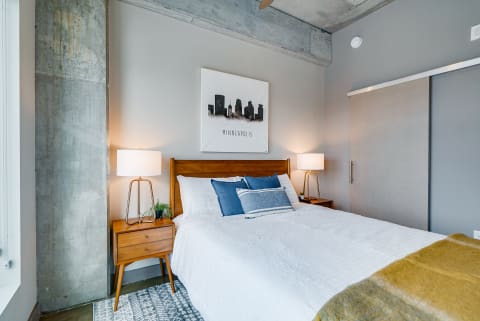 A contemporary bedroom featuring a queen bed, wooden nightstands, skyline artwork, and an industrial column.
