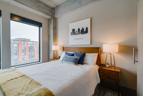 A modern bedroom with a skyline artwork, cozy bed, and industrial design elements.