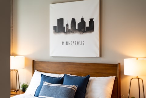 A cozy bedroom with a skyline art depicting Minneapolis and a wooden bed.