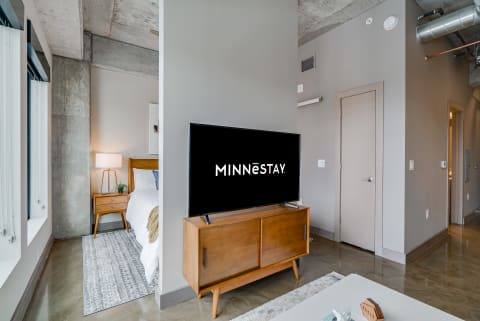 Modern living space with a bedroom and television showing MINNēSTAY logo.