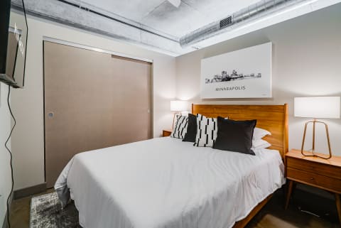 Modern bedroom with white bed, black and white patterned pillows, and wood nightstand.