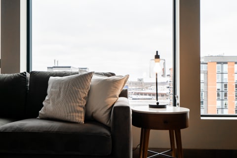 Cozy living room corner with gray sofa, patterned pillows, and a lamp by the window.