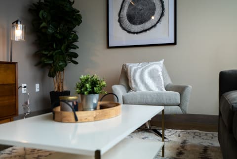 Cozy living area with a grey armchair, white coffee table, and indoor plant.