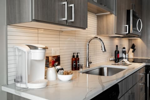 A sleek modern kitchen countertop with a coffee maker, marble sink, and decorative items.