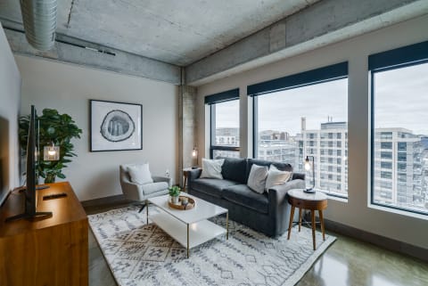 A contemporary living room featuring a gray sofa, armchair, and large windows overlooking a cityscape.