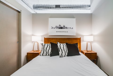 Contemporary bedroom with a bed, decorative pillows, and wall art of Minneapolis skyline.