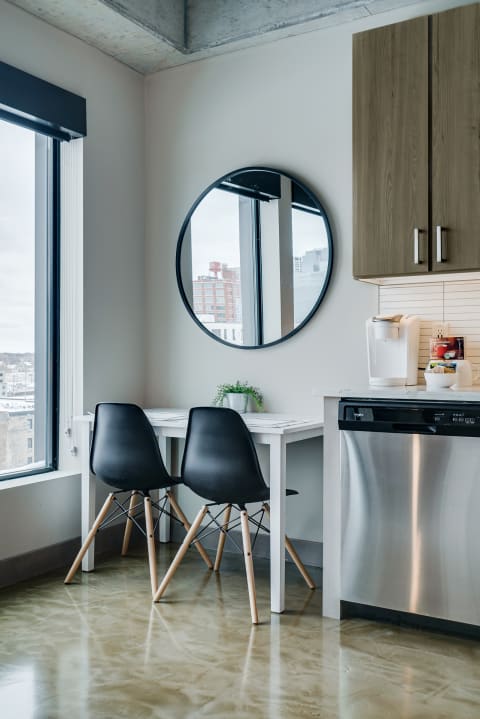 A minimalist kitchen area featuring a white table, black chairs, and a round mirror.