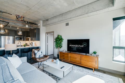 Stylish living room with exposed concrete ceiling, gray sofa, and modern kitchen in the background.