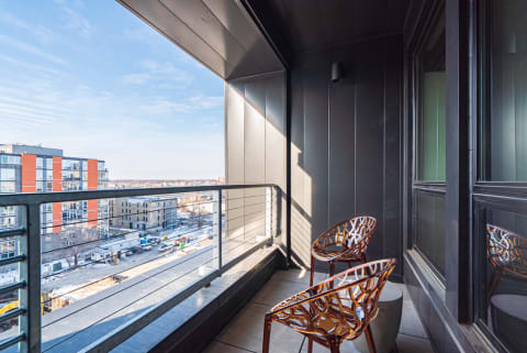 A sleek balcony with two decorative chairs, overlooking urban buildings and a clear sky.