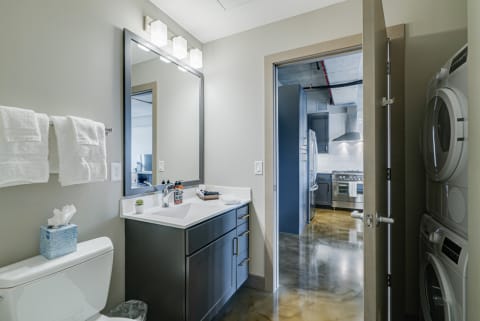 Modern bathroom with a sleek black vanity, white countertop, and adjoining kitchen area.