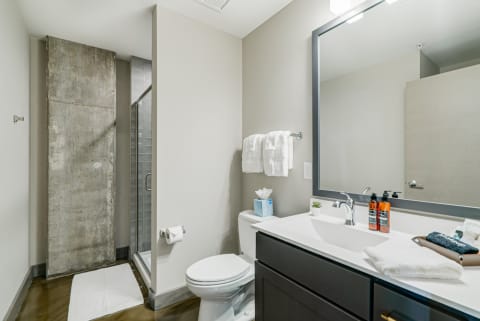 A minimalist bathroom featuring a glass shower, concrete wall, and dark wooden vanity with toiletries.
