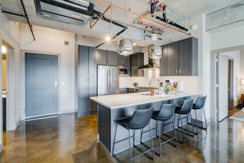Modern kitchen with gray cabinets, marble countertops, and black bar stools.