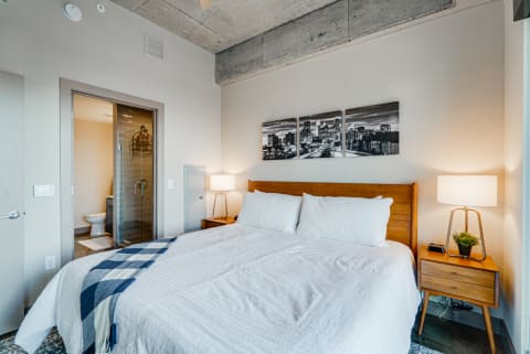 Cozy bedroom with a queen-sized bed, nightstands, and city skyline artwork.