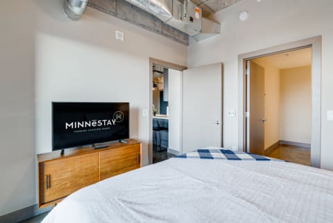 A modern bedroom with a bed, flat-screen TV, and industrial decor elements.