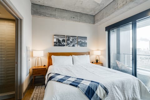 A modern bedroom with a king-sized bed, urban artwork, and large windows overlooking the city.