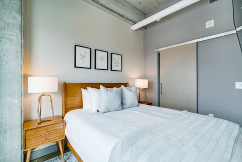 A cozy bedroom featuring a wooden bed with decorative pillows, nightstands, and botanical art on the wall.