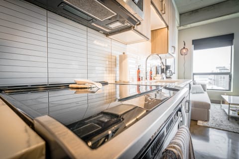 Modern kitchen with a black cooktop and light grey tiled backsplash, showcasing a cozy living area in the background.