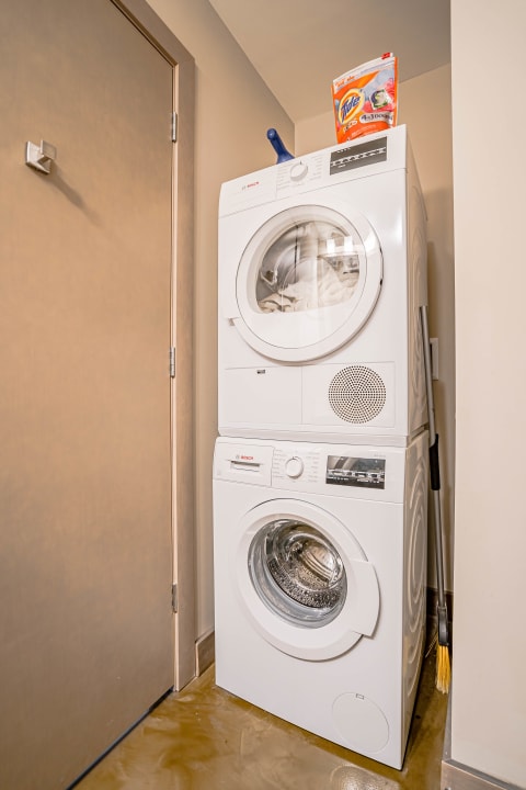 A stacked white washer and dryer in a laundry space with a box of Tide detergent on top.
