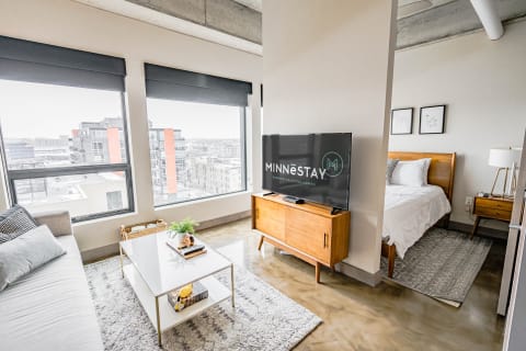 A modern studio apartment with a sofa, coffee table, and television displaying the logo for MINNESTAY.